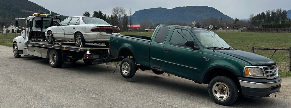 Tow truck hauling a junk car and towing a scrap pickup truck
