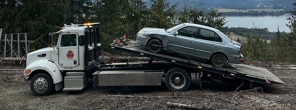 Scrap car being loaded onto a flat deck tow truck