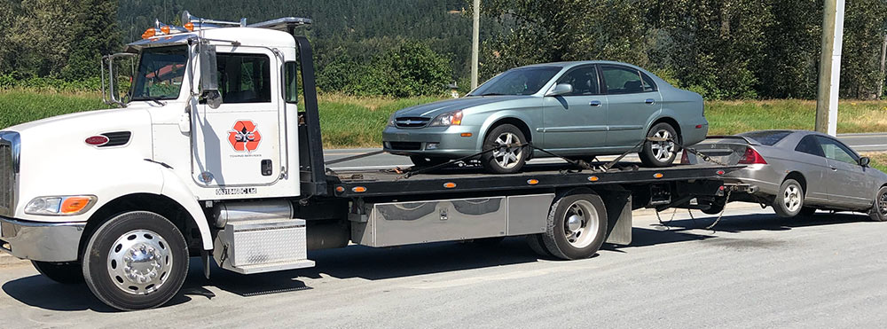 Flat deck tow truck removing two scrap cars